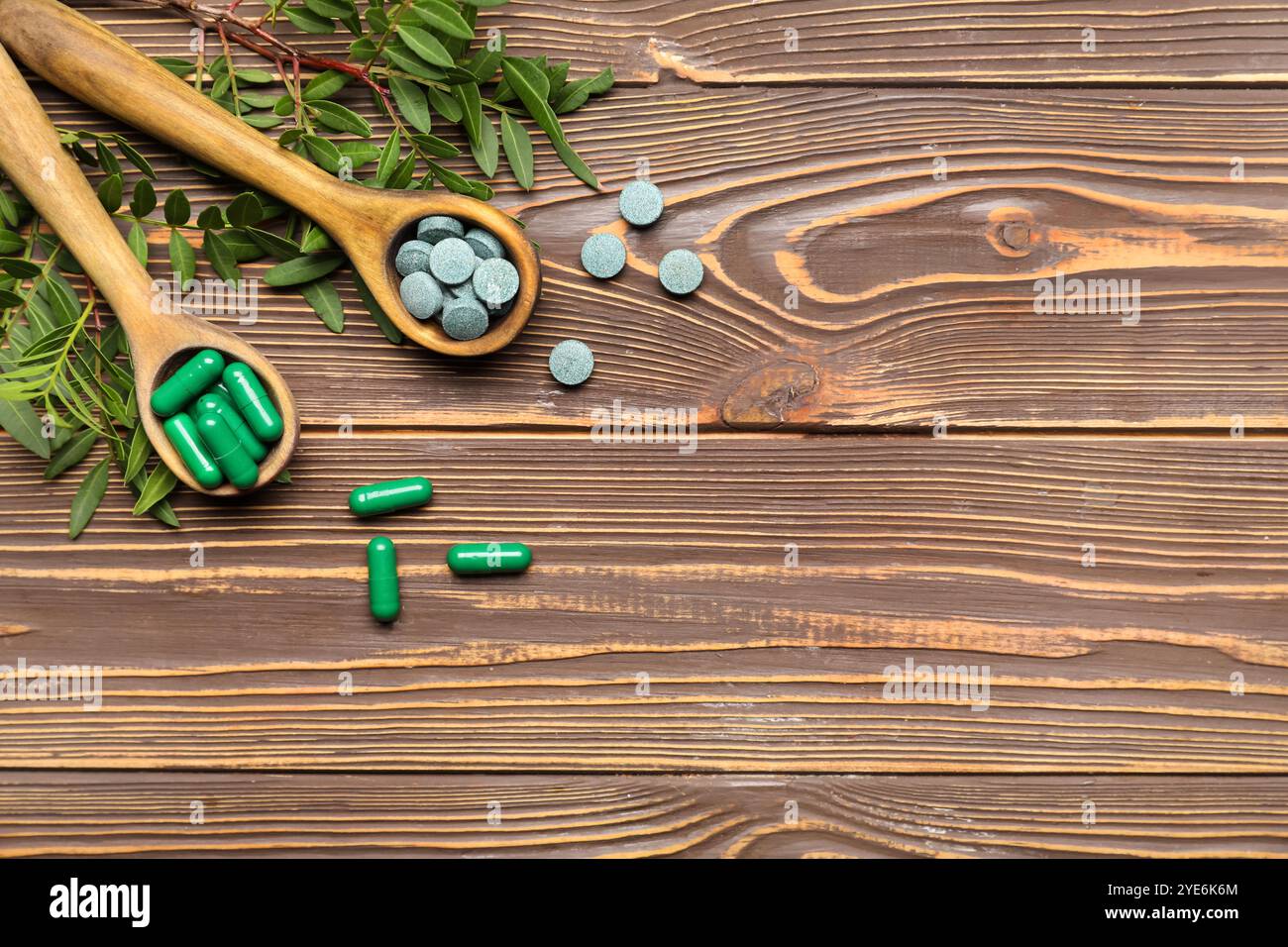 Spoons with pills and plants on wooden background Stock Photo
