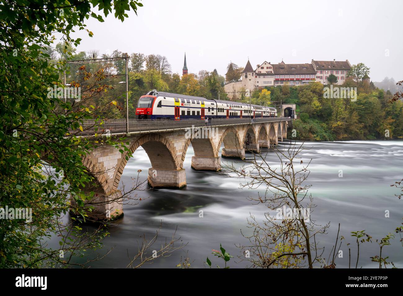 PHOTO-COMPOSITION long and short exposure mixture: Train passing over the Rheinbrücke bei Laufen bridge at the beautiful Swiss Rhine Falls, seen during the fall time. Schaffhausen *** PHOTO COMPOSITION long and short exposure mixture Train passing over the Rheinbrücke bei Laufen bridge at the beautiful Swiss Rhine Falls, seen during the fall time Schaffhausen Stock Photo