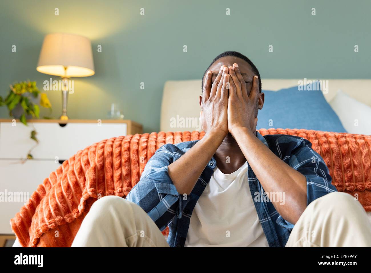 Stressed African american man sitting on floor at home, covering face with hands Stock Photo