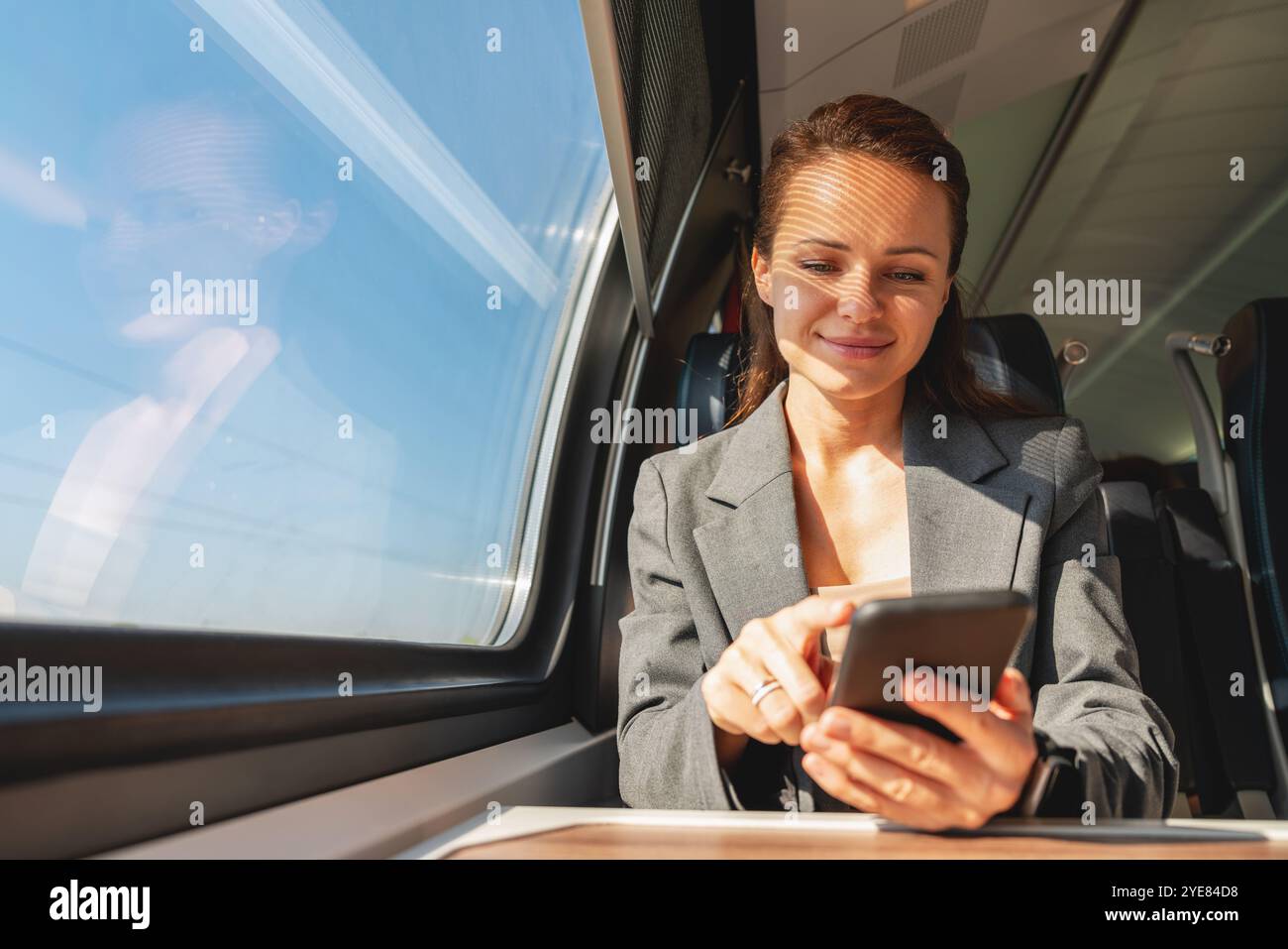 Business travel and commuting. Woman in business attire traveling by modern train and using her smartphone. Stock Photo