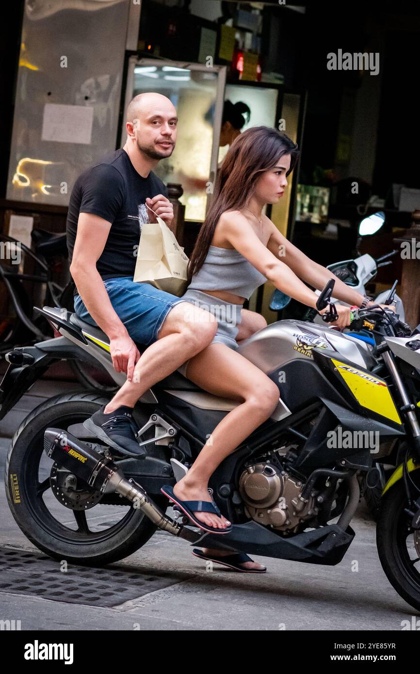 A western man sat at the back of the scooter or motorbike as his Thai partner drives along Soi Buakhao, Pattaya Thailand. Stock Photo