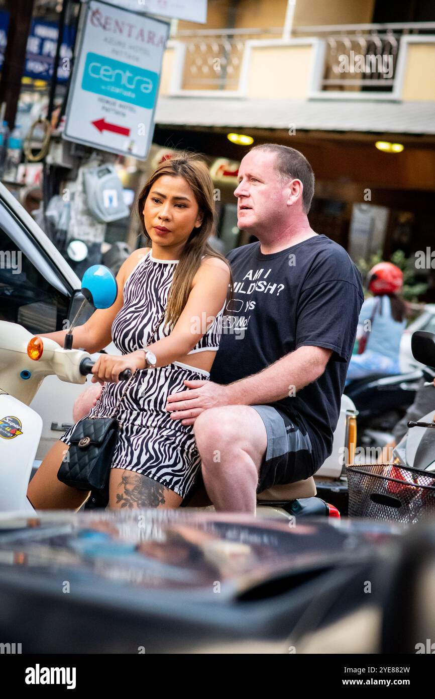 A western man sat at the back of the scooter or motorbike as his Thai partner drives along Soi Buakhao, Pattaya Thailand. Stock Photo