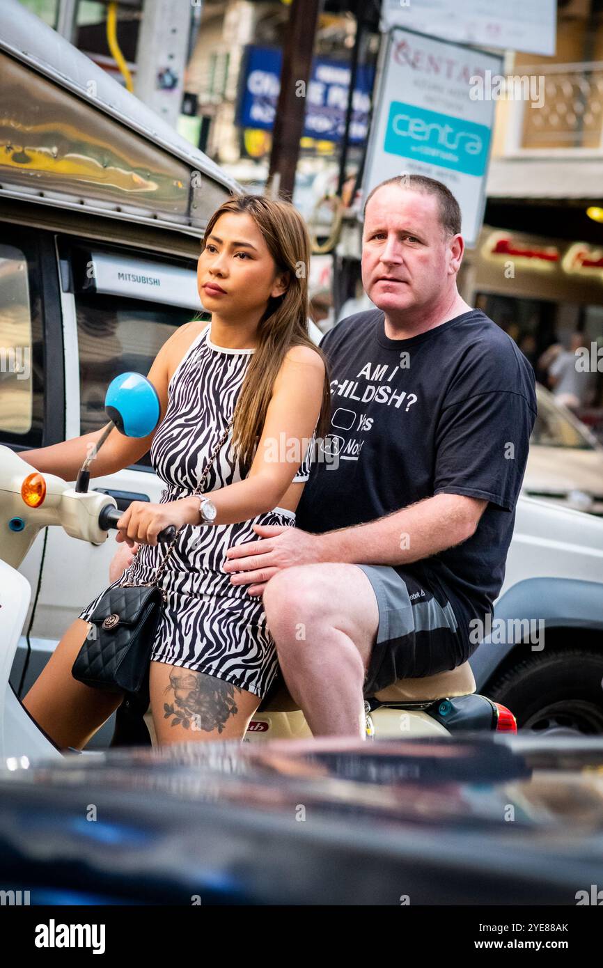A western man sat at the back of the scooter or motorbike as his Thai partner drives along Soi Buakhao, Pattaya Thailand. Stock Photo
