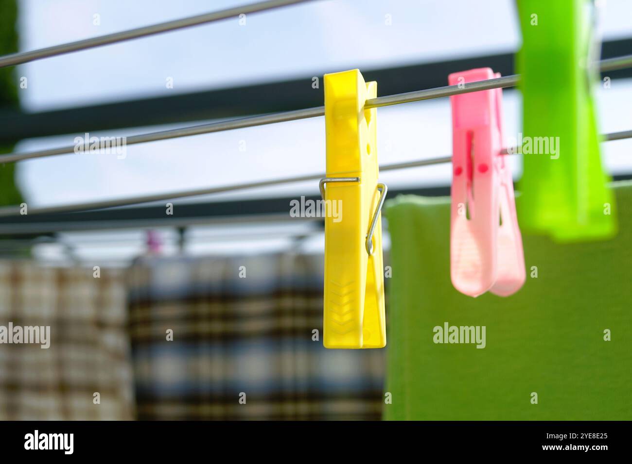 Drying laundry on a sunny day: a close-up of colorful plastic clothespins hanging on rods of an outdoor drying rack against a background of clothes Stock Photo