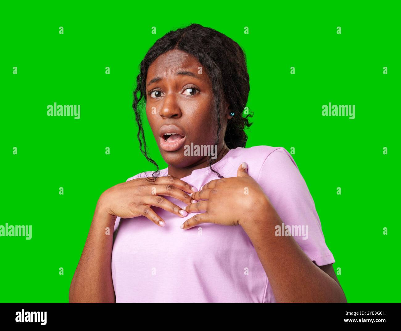 Surprised young woman against a vibrant green background expressing astonishment or shock Stock Photo