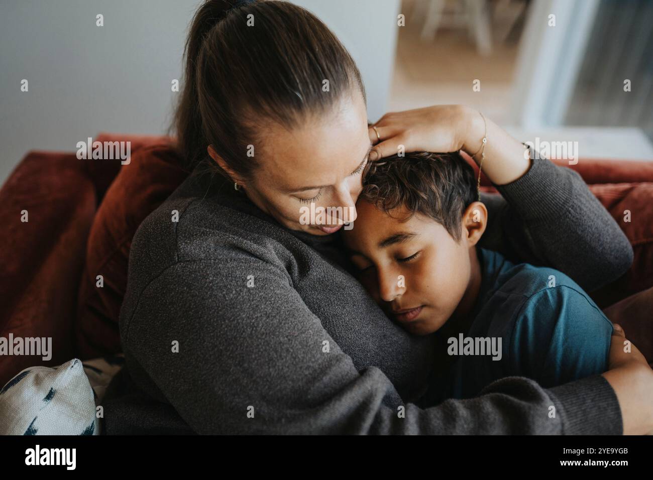 Mother embracing son while sitting on sofa at home Stock Photo