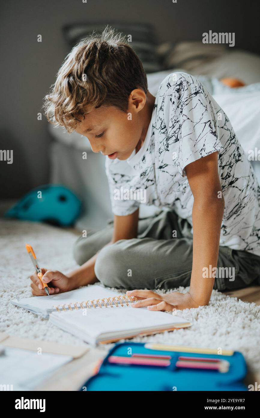 Focused boy doing homework while sitting on carpet at home Stock Photo