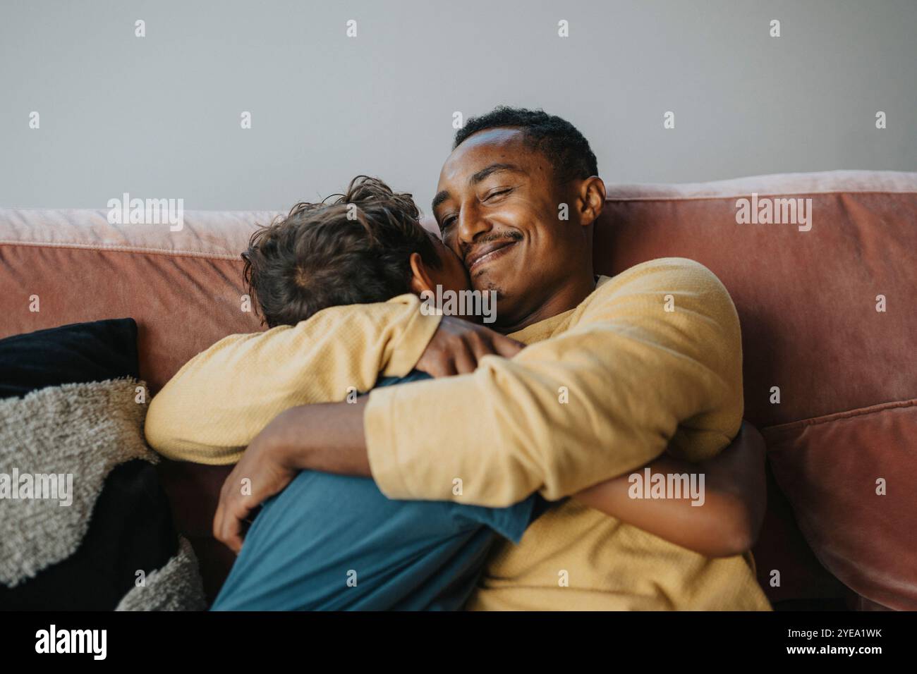 Smiling father embracing son while sitting on sofa at home Stock Photo
