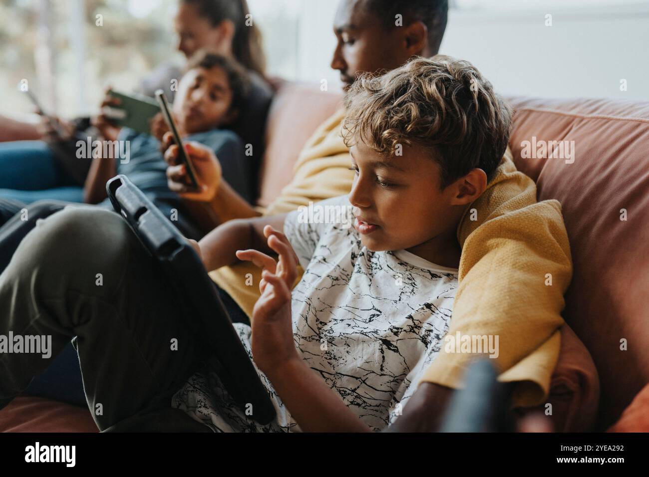 Curly haired boy using tablet PC while sitting with father on sofa at home Stock Photo