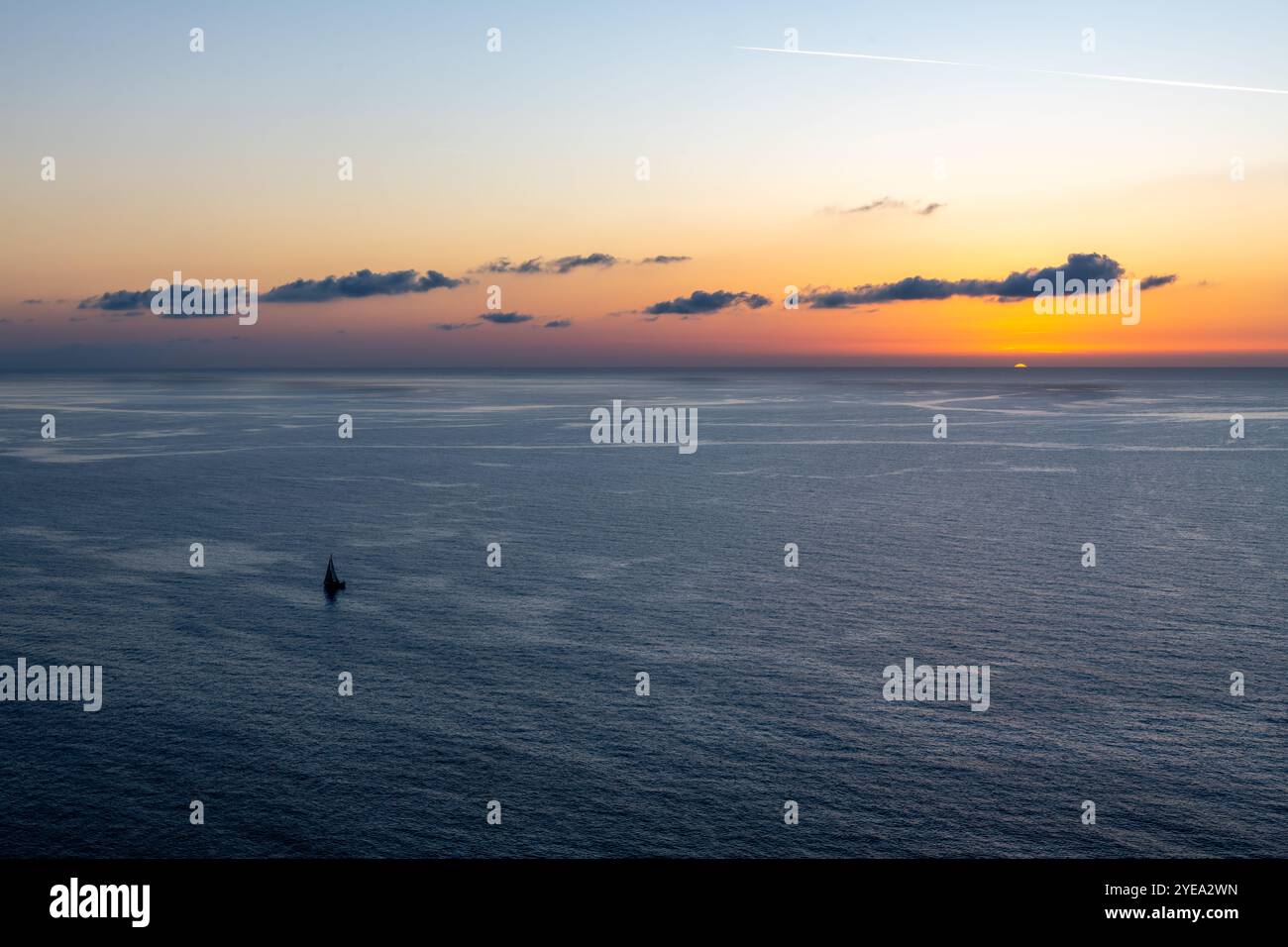 A lone yacht sailing in the vast ocean in sunset. Stock Photo