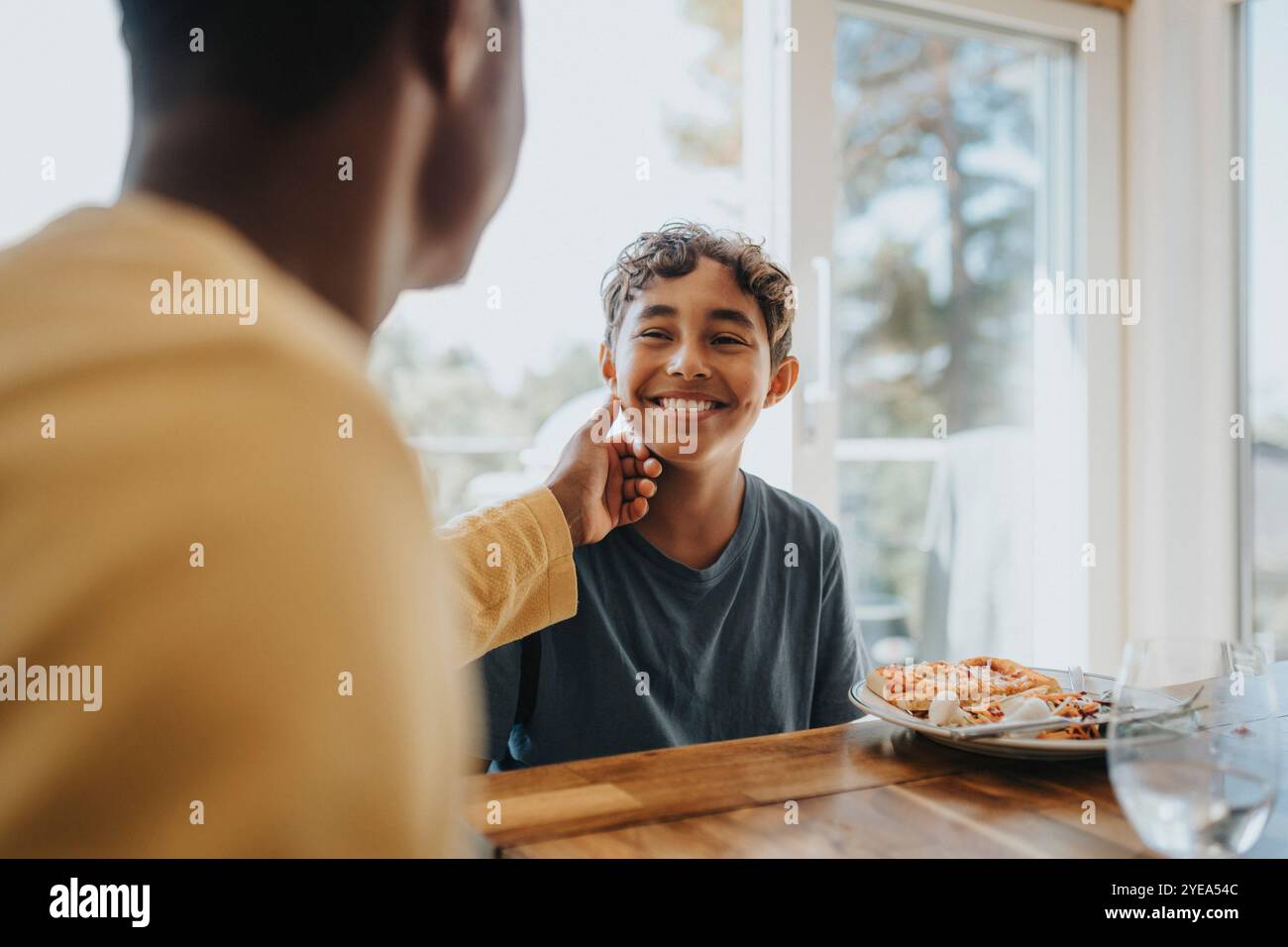 Father touching cheek of son sitting for lunch at dining table Stock Photo