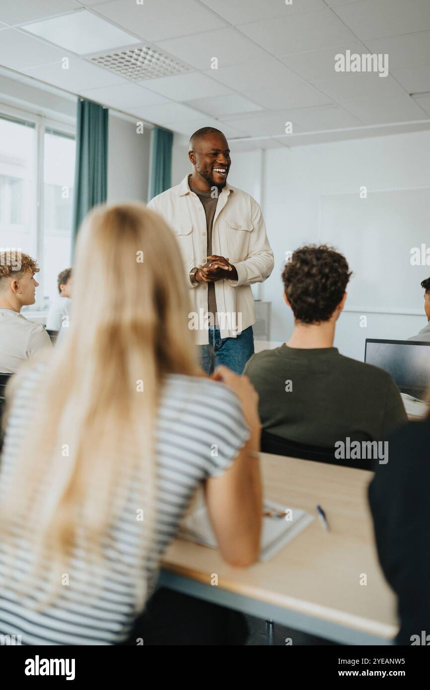 Happy male teacher gesturing while discussing with high school students in classroom Stock Photo
