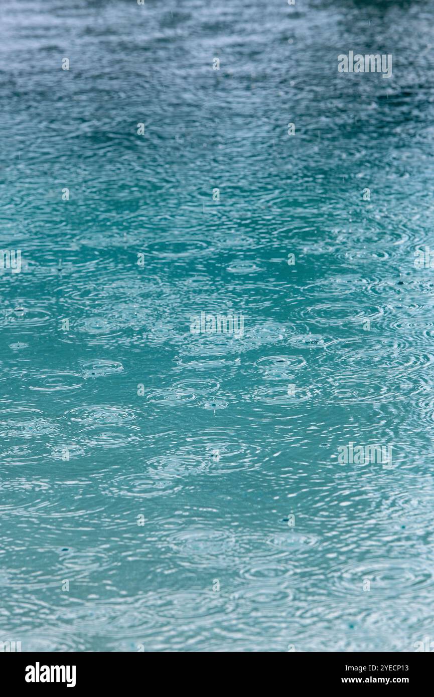 raindrops falling on a swimming pool creating abstract pattern suitable for use as a backdrop or background Stock Photo