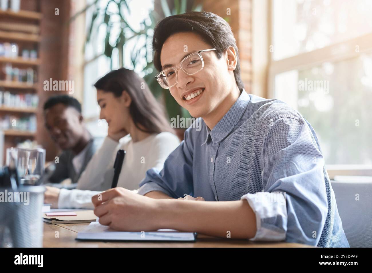 Smiling asian guy taking notes while business meeting with colleagues Stock Photo