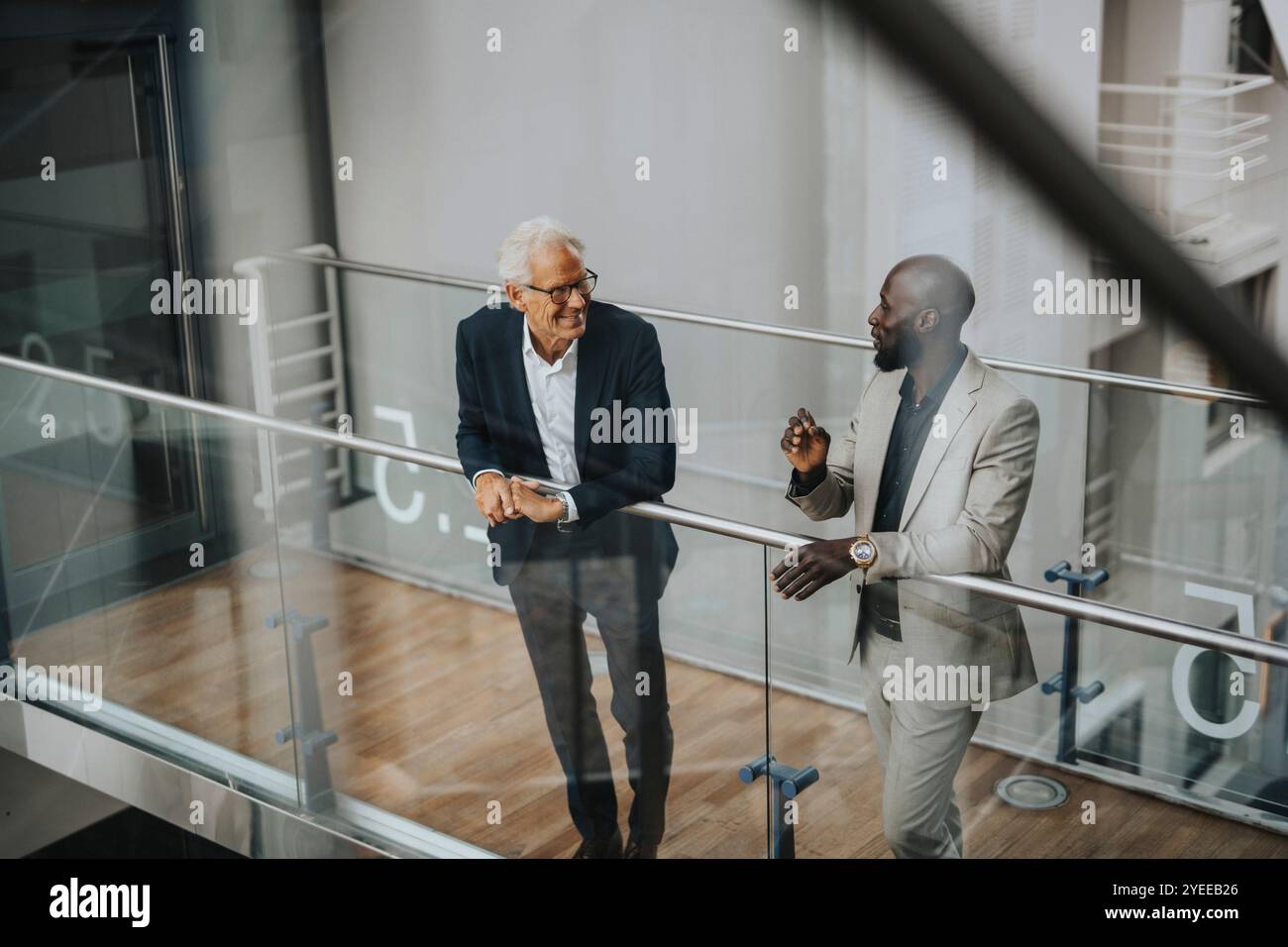 Smiling businessmen discussing while standing by glass railing Stock Photo