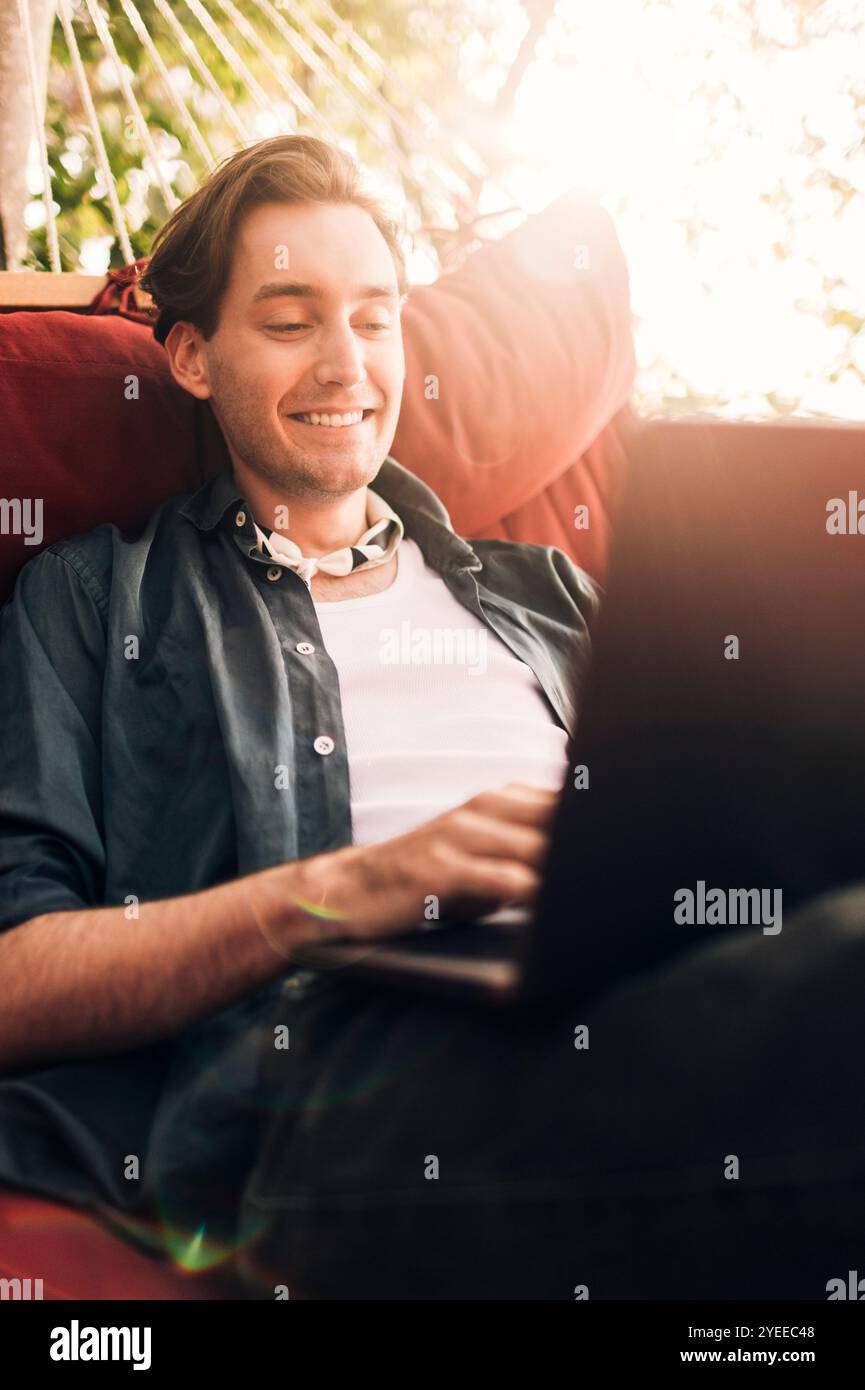 Smiling young man using laptop while sitting in hammock Stock Photo