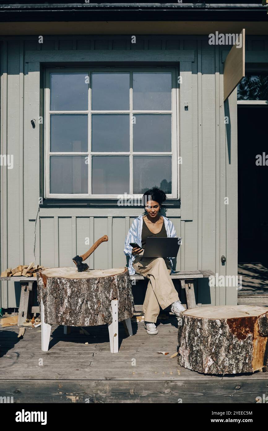 Female designer using laptop while sitting on bench outside workshop Stock Photo