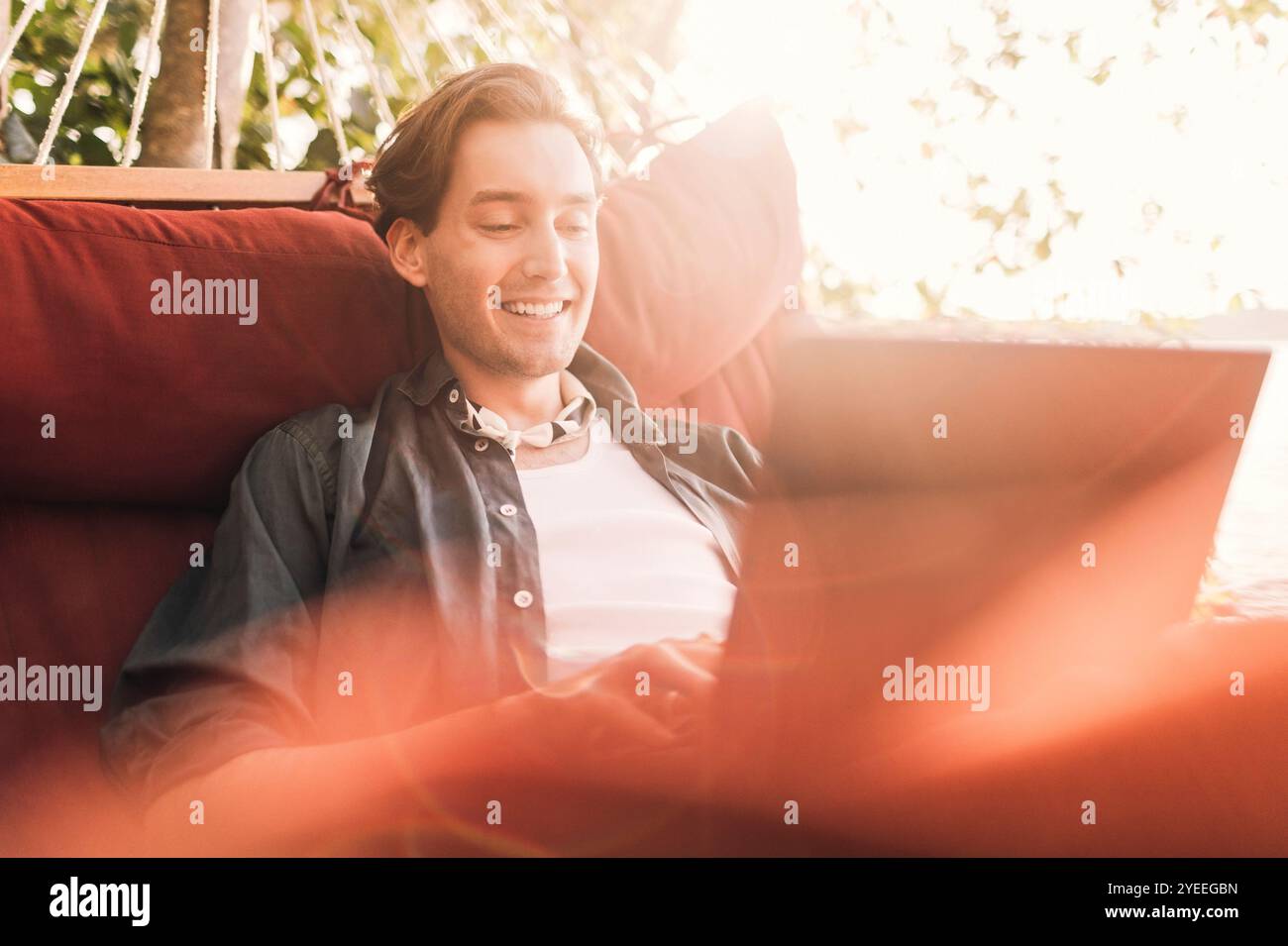 Smiling young man using laptop sitting in hammock Stock Photo