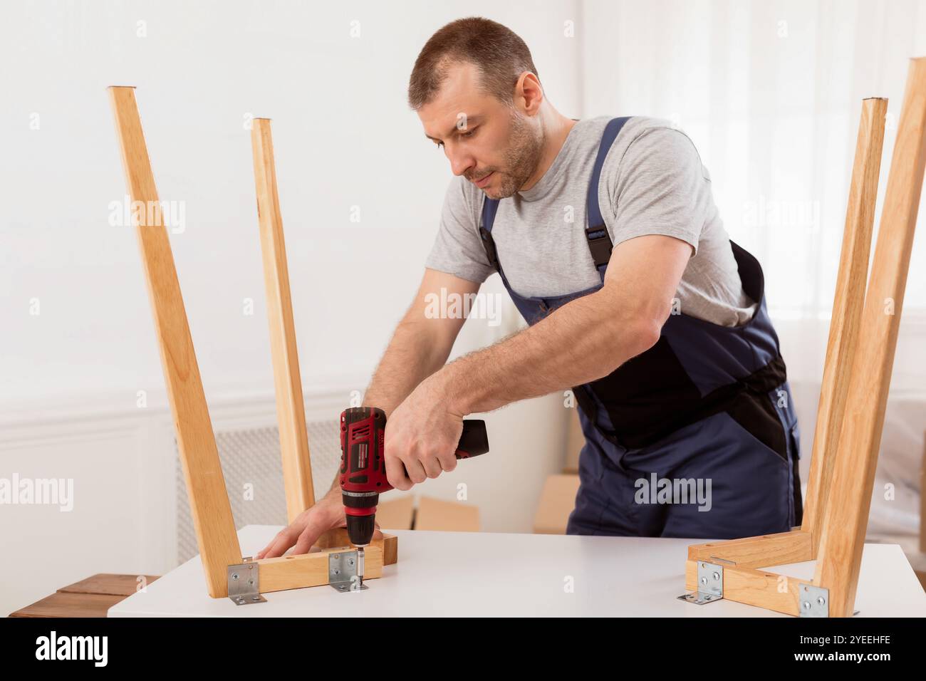 Male Carpenter Using Electric Drill Assembling Wooden Table In Studio Stock Photo