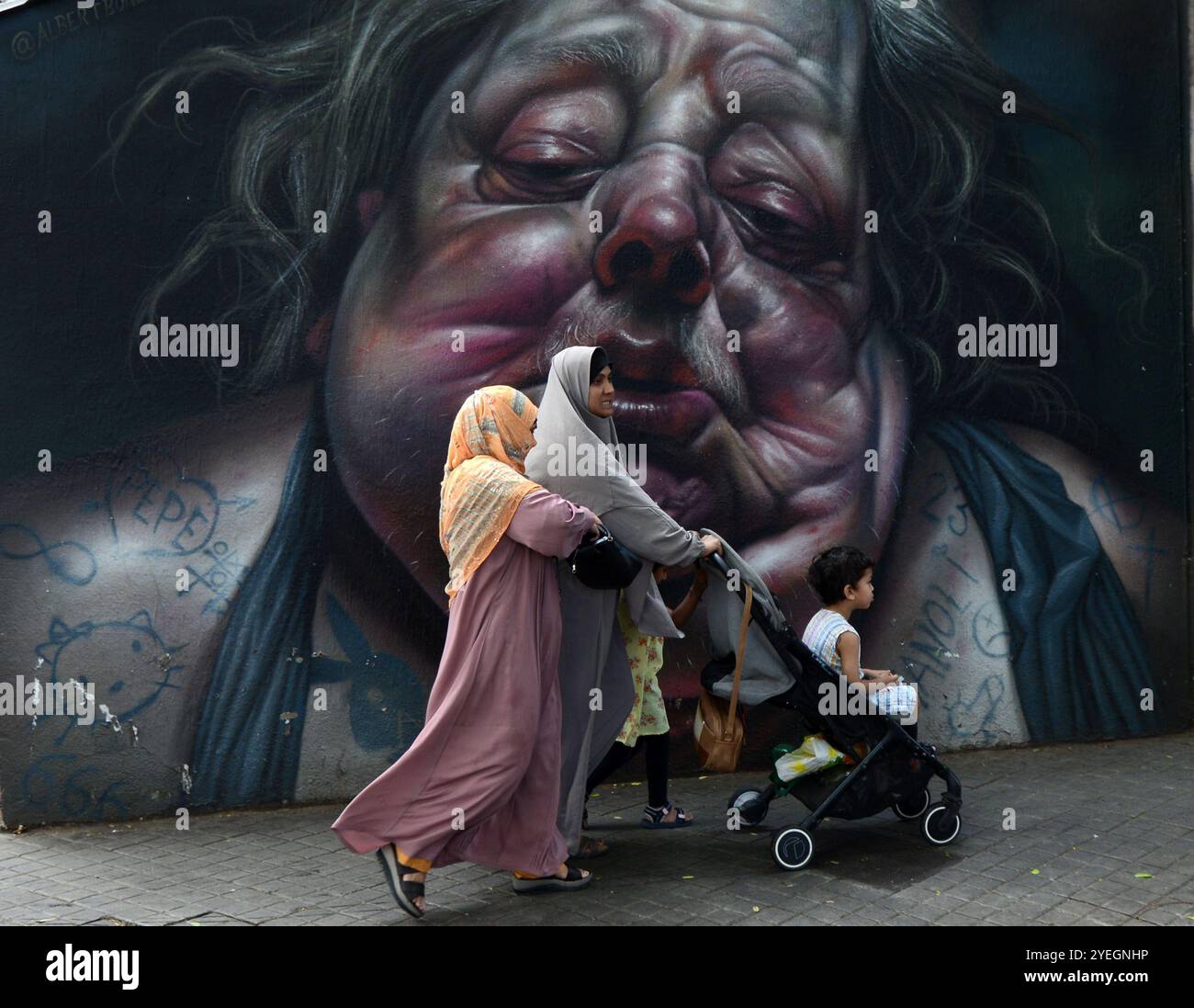 Muslim women walking by a beautiful wall mural on the Graffiti wall on Carrer Nou de la Rambla in Barcelona, Spain. Stock Photo