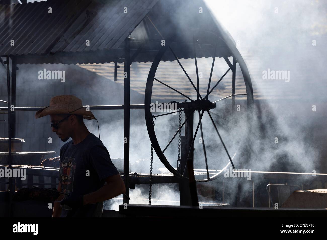 Oak Glen, California, USA - October 29, 2023: The BBQ pit master crosses in front of the smokey barbecue at the Los Rios Rancho. Stock Photo