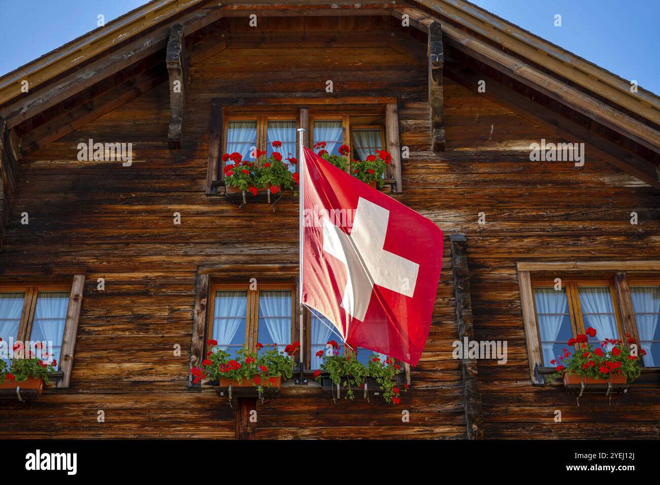 Beautiful Old Town with a Wood House with Flower and Swiss Flag in a Sunny Summer Day in Andermatt, Uri, Switzerland, Europe Stock Photo