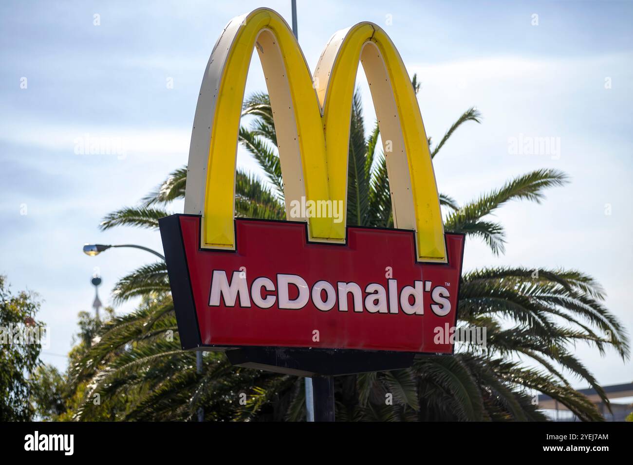 A McDonald's sign with the iconic golden arches, standing in front of palm trees, photographed on a sunny day, showcasing the brand's recognizable log Stock Photo