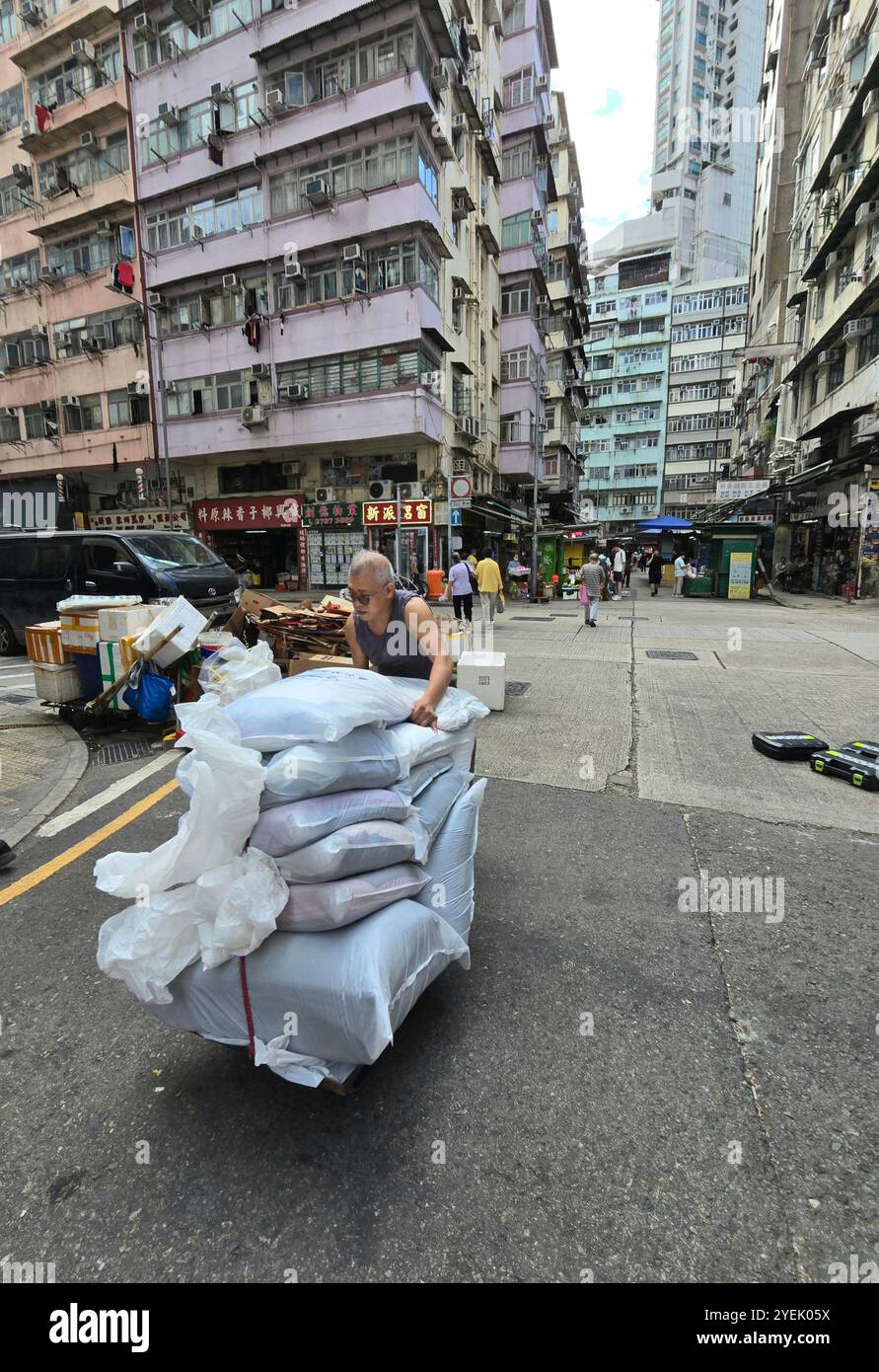 A man pushing a trolley loaded with heavy bags at the market on Fife street in Mong Kok, Kowloon, Hong Kong. - Smartphone Captured Stock Image