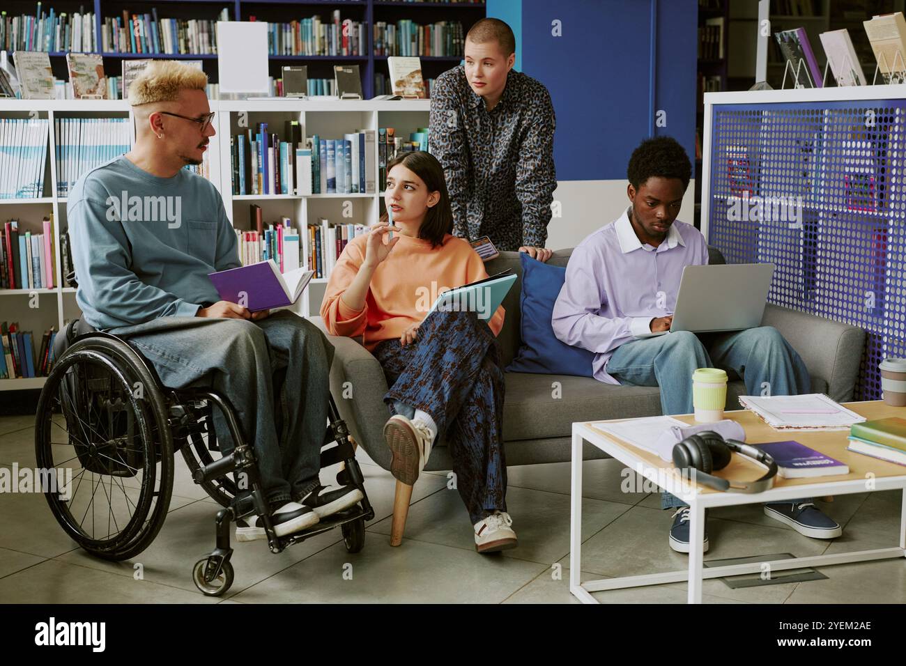 Group of diverse students collaborating in modern library environment discussing projects, sharing ideas seated on sofas and using laptops for studying, learning together Stock Photo