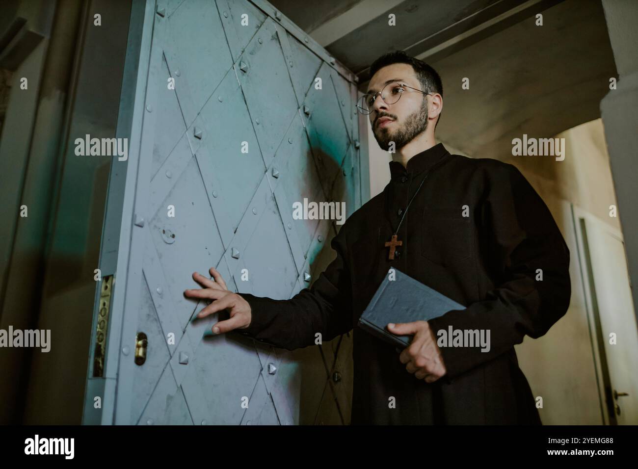 Low angle shot of young Caucasian priest in black robe with wooden ...