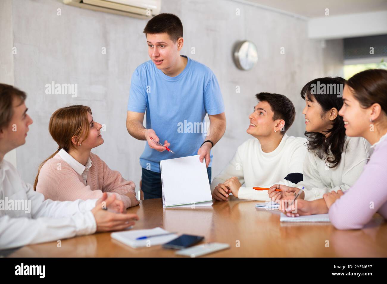 Cheerful young student discussing learning assignment with coursemates Stock Photo