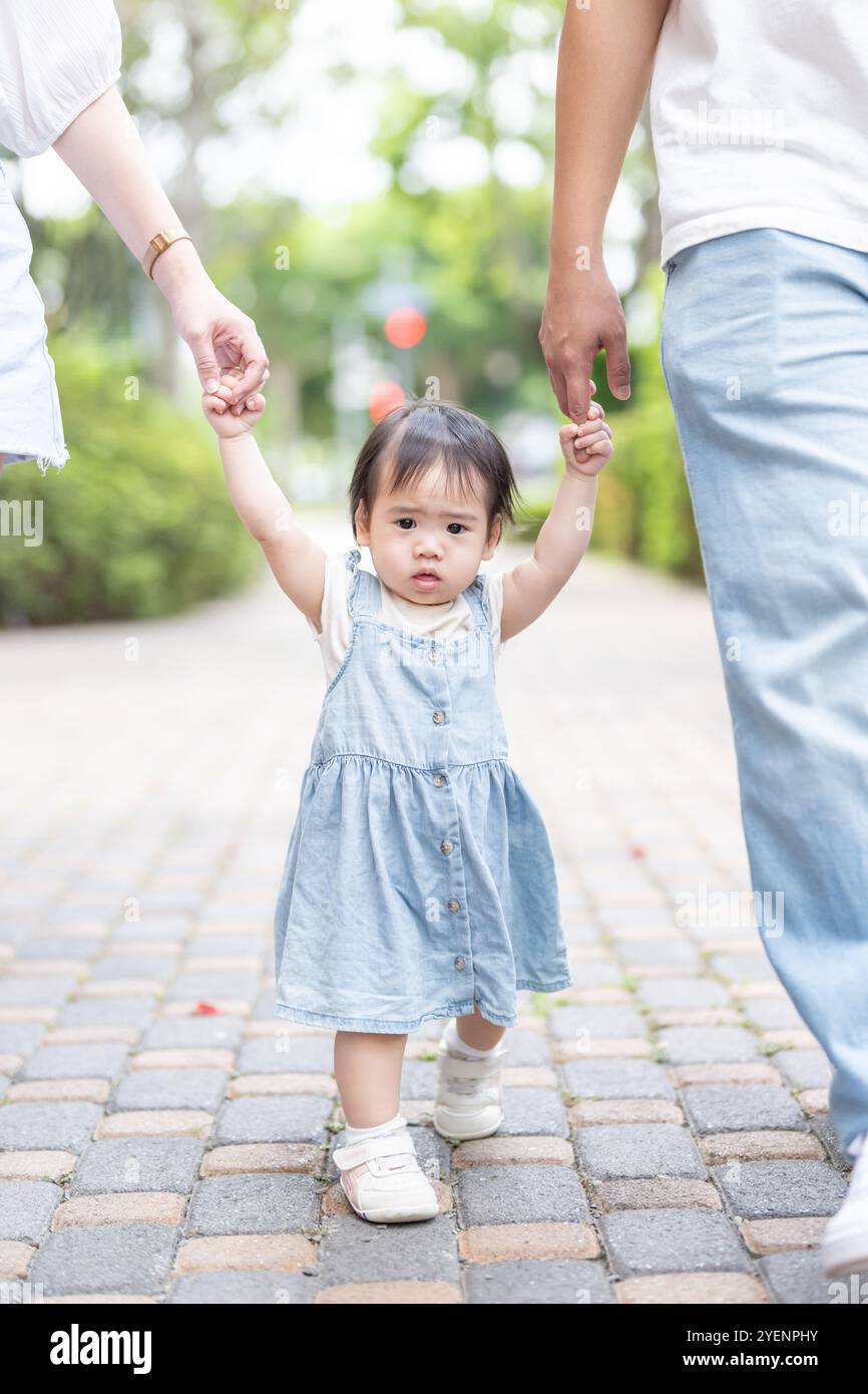 A 1 year old Taiwanese girl walking hand in hand with her parents, a ...