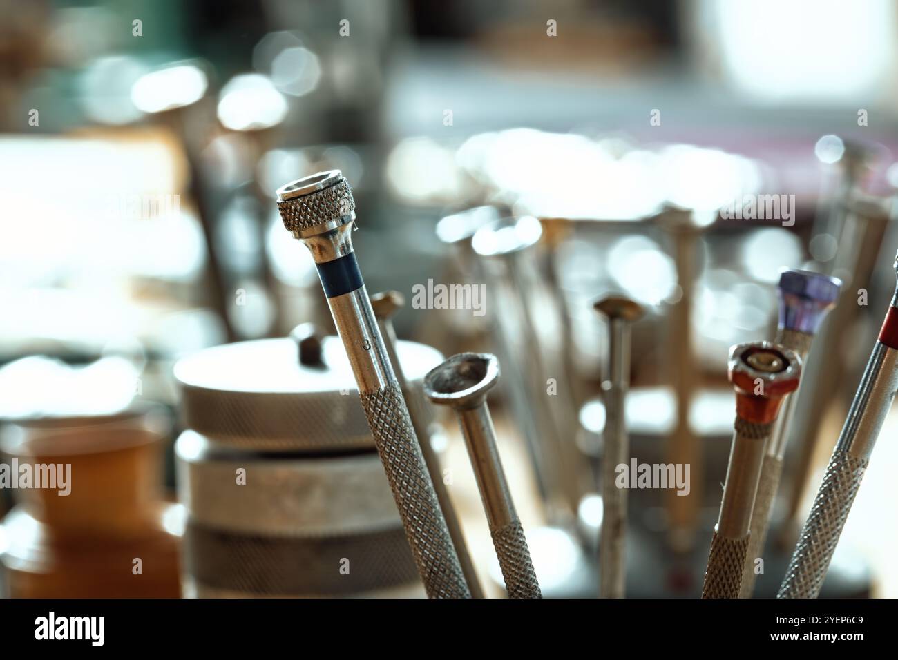 On a workbench, a set of precision screwdrivers stands upright. Each tool has a knurled handle and colored tip, indicating an organized setup for watc Stock Photo