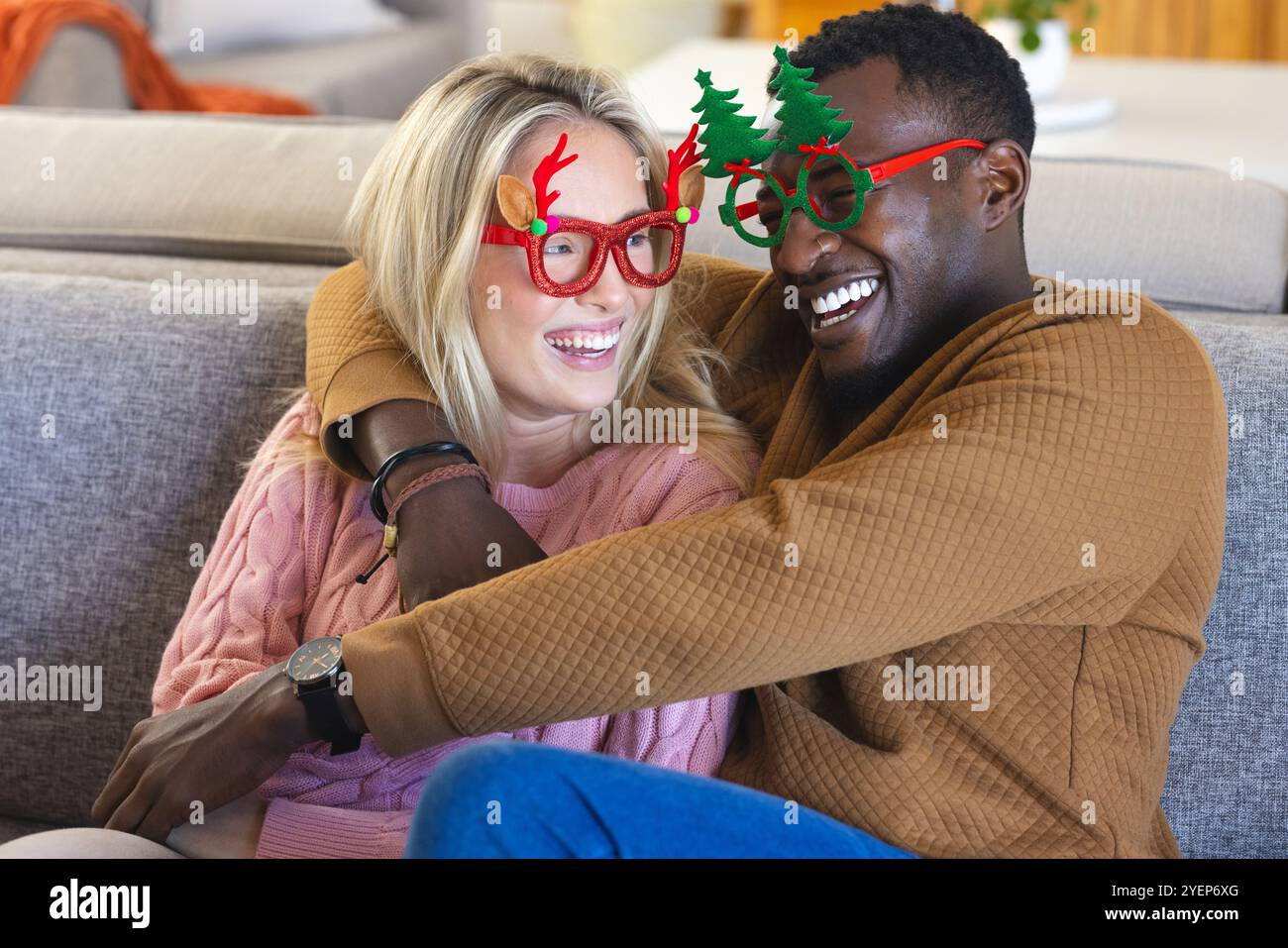 Christmas time, smiling multiracial couple wearing festive glasses, at home. celebration, winter, together Stock Photo