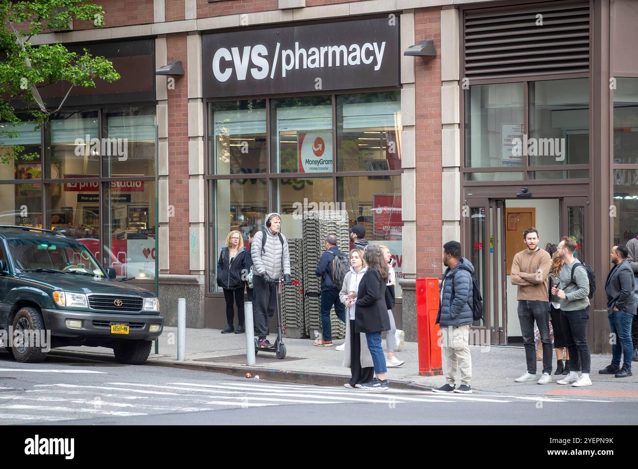 The image depicts a group of people standing outside a CVS pharmacy ...