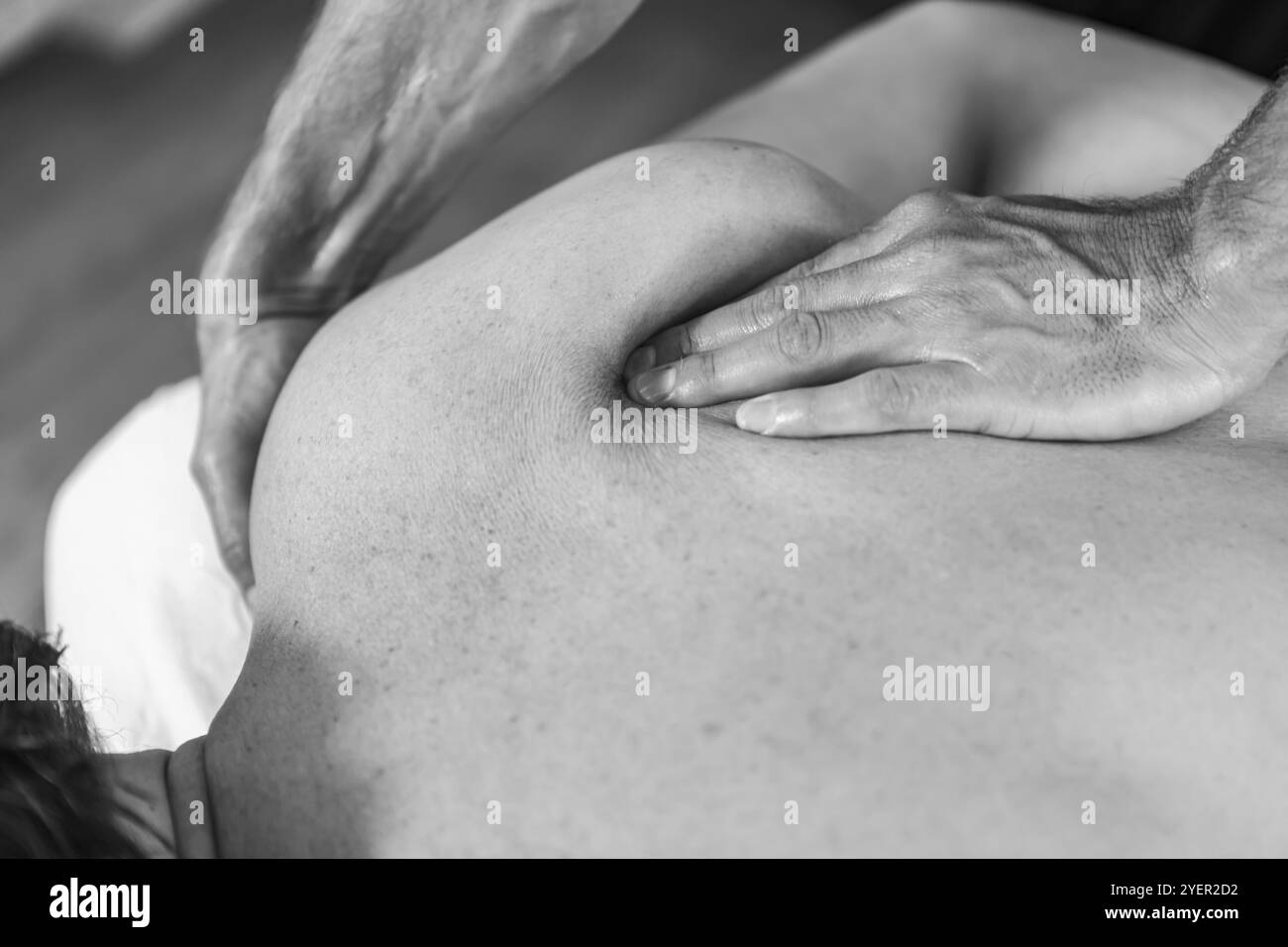 Black and white image of professional masseur-therapist hands giving a massage. Close-up view of young sportsman receiving a treating back massage Stock Photo