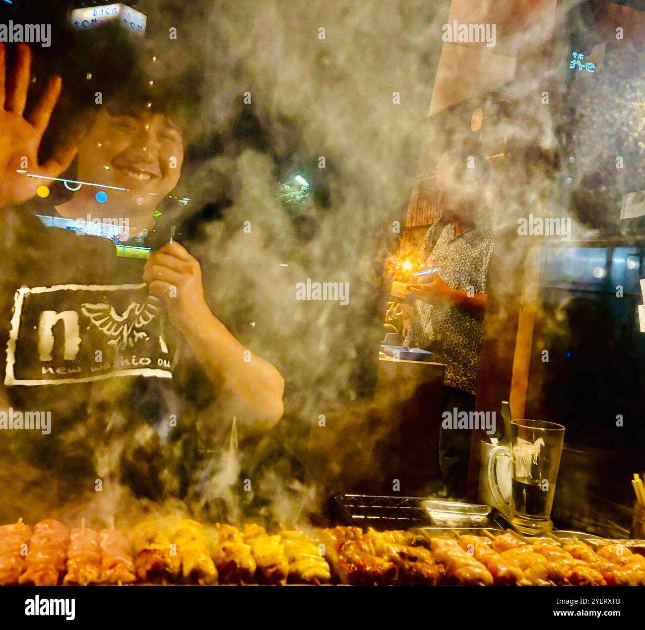 A young Japanese man grilling skewers at the Washio Yakitori Izakaya restaurant in Chuocho, Kagoshima, Japan. - Smartphone Captured Stock Image