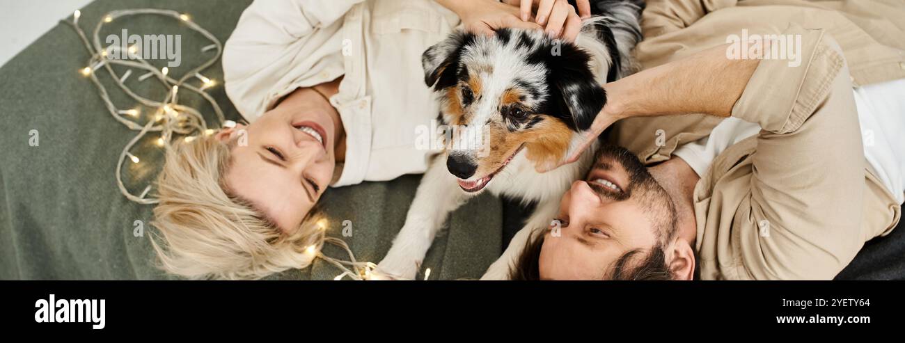 A happy couple shares a playful moment on their cozy floor surrounded by soft lights and their dog. Stock Photo