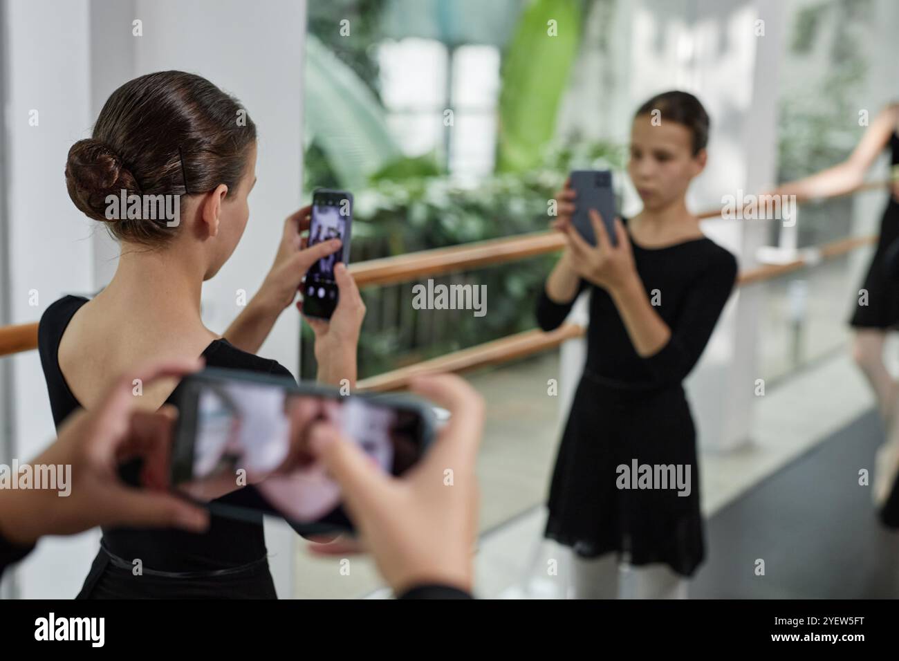 Rear view of little girl with hair styled in bun taking photo in mirror ...