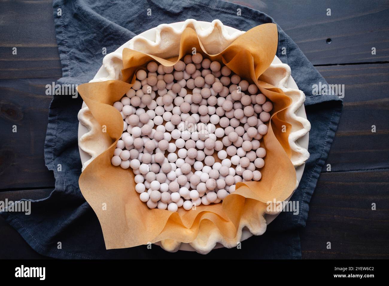 Preparing to Blind Bake a Fluted Pie Crust: Pie crust lined with parchment paper and filled with ceramic pie weights for blind baking Stock Photo