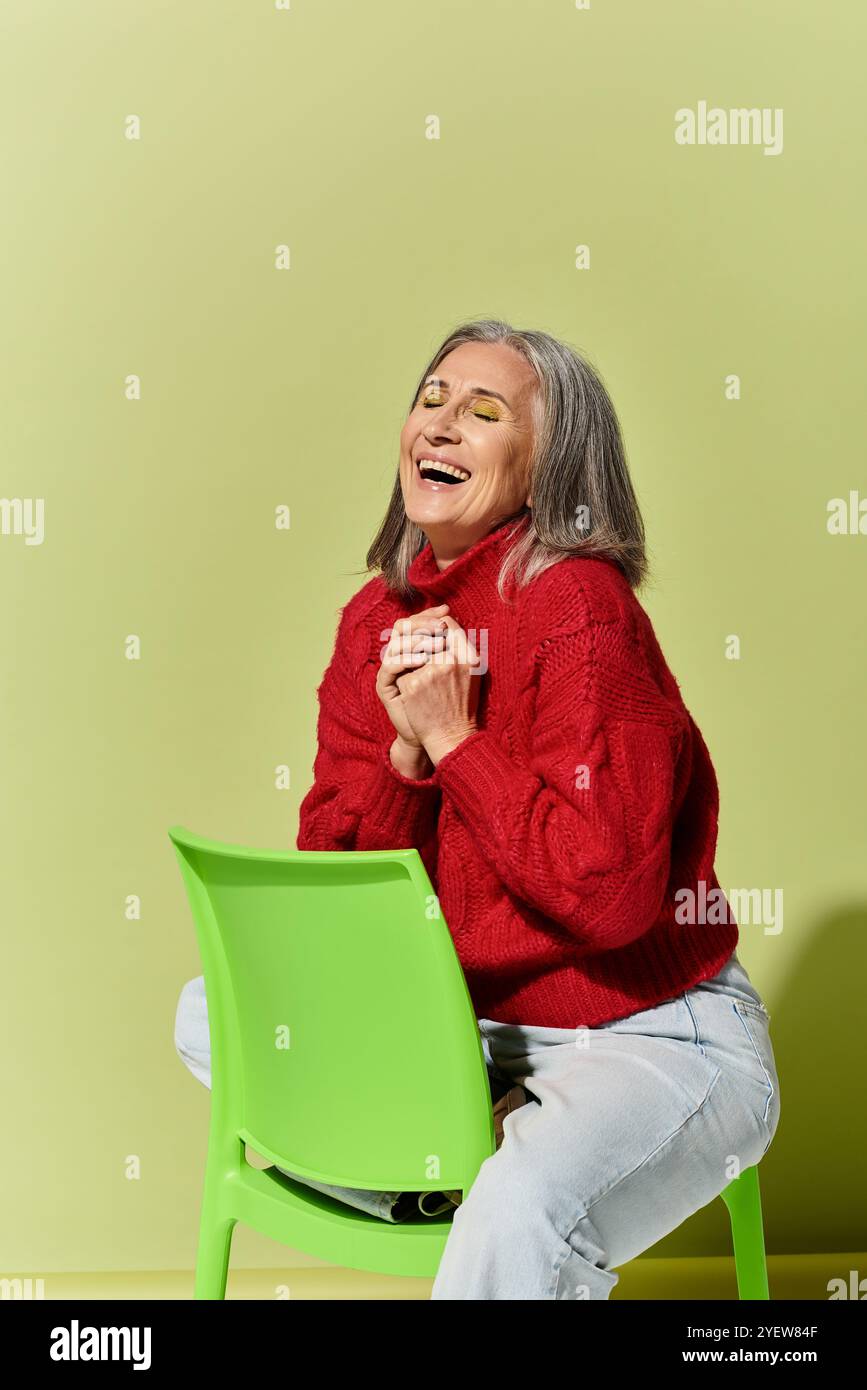 Embracing the warmth of winter, a mature woman beams with joy in her red sweater, set against a bright green hue. Stock Photo