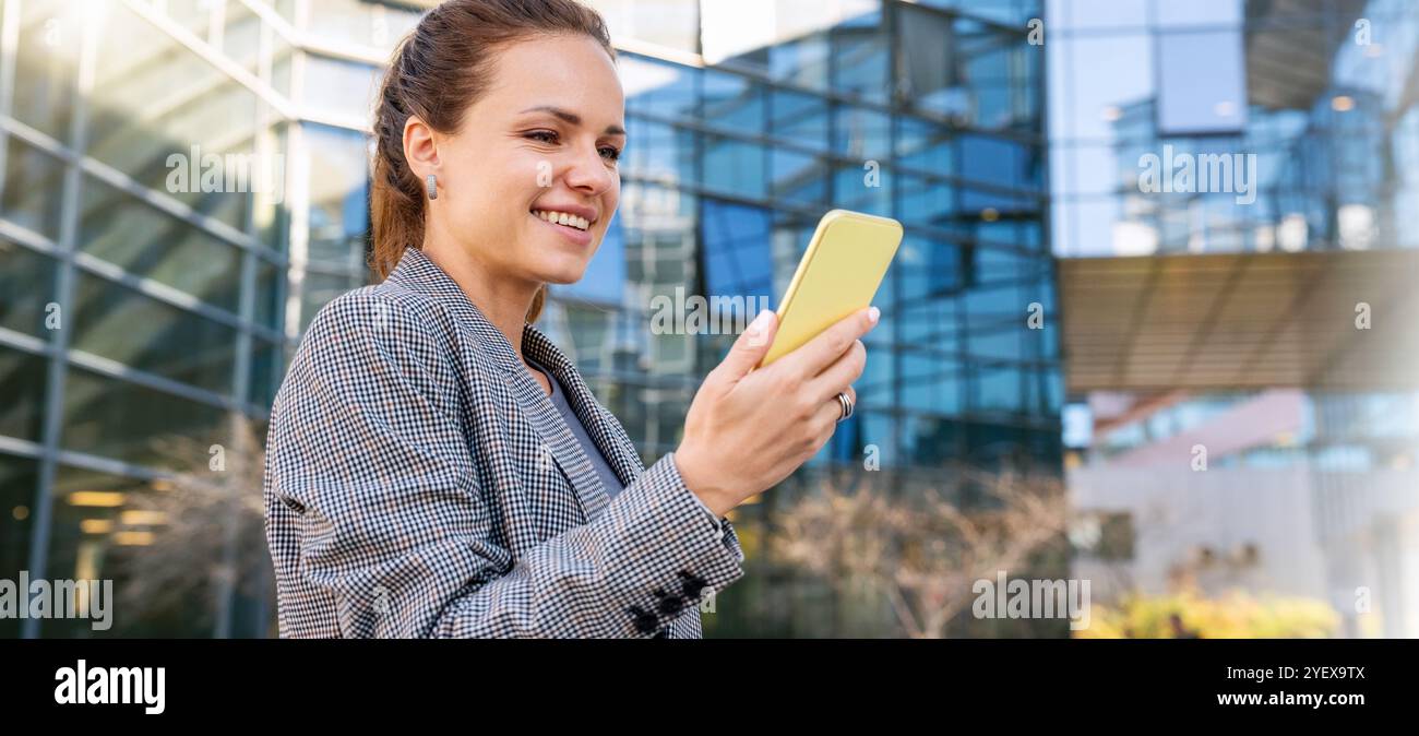 Corporate networking. Businesswoman communicate with colleges using her smartphone. Female business person using smartphone outdoors of the office bui Stock Photo