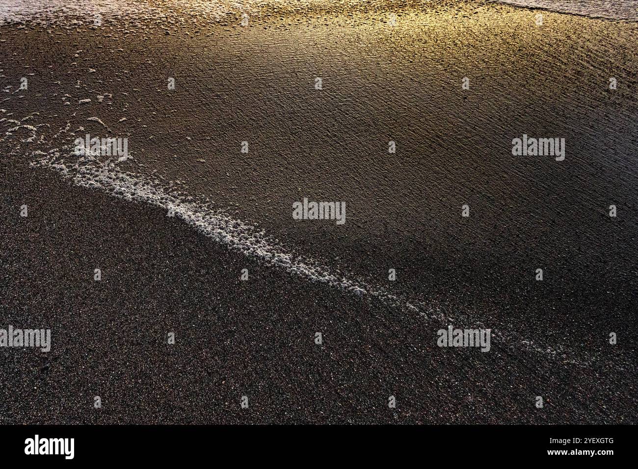 Waves on a sandy beach forming beautiful colored patterns in the glow ...