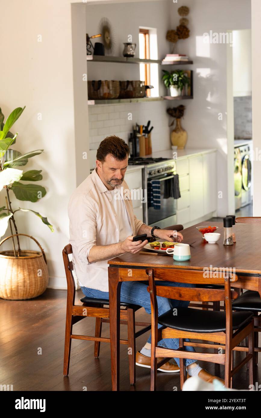 senior man using smartphone at home while enjoying breakfast at dining table Stock Photo