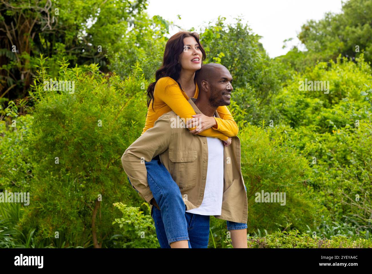 Happy multiracial couple enjoying piggyback ride in lush green park ...