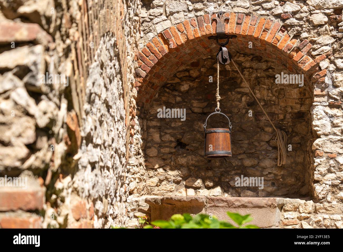 Old stone well with wooden bucket in front of a stone wall Stock Photo