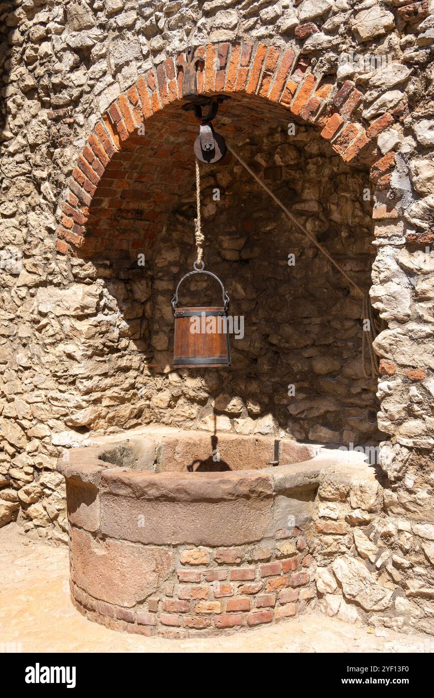 Old stone well with wooden bucket in front of a stone wall Stock Photo