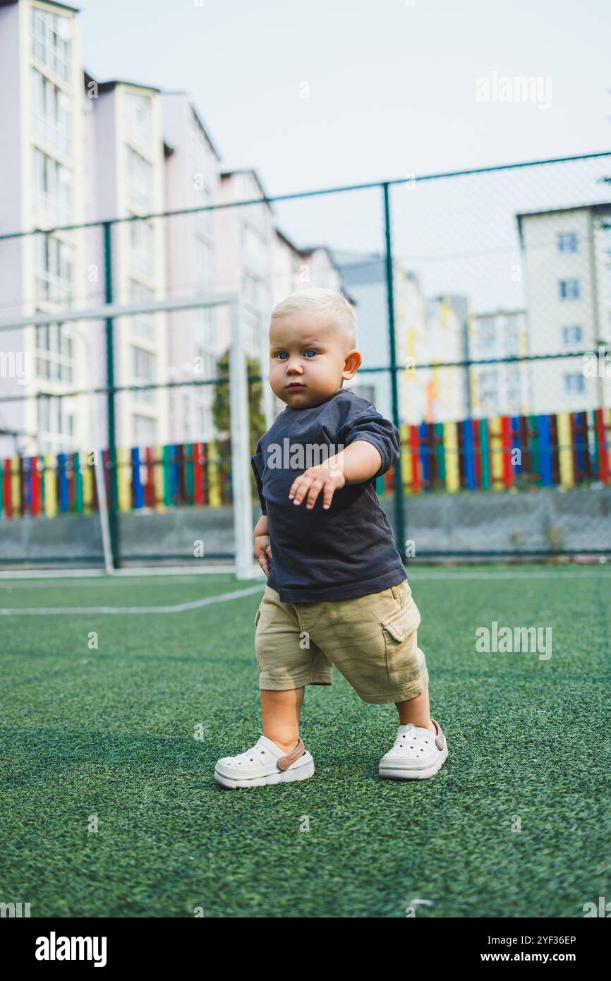 Joyful 1-year-old boy running on the stadium in the park. Green grass ...