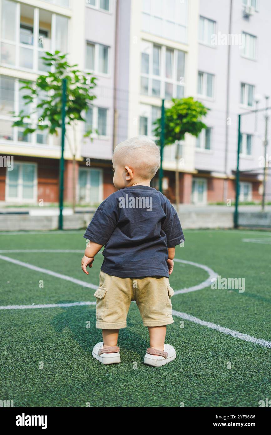 Joyful 1-year-old boy running on the stadium in the park. Green grass ...