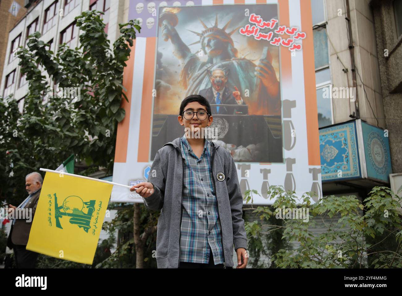 Tehran, Iran. 3rd Nov, 2024. An Iranian boy holds a Hezbollah flag while standing in front of a large banner featuring an image of Benjamin Netanyahu, the Prime Minister of Israel, during an anti-US rally marking the 45th anniversary of the U.S. Embassy takeover in front of the former embassy building in Tehran. On 4 November 1979, Iranian students seized the U.S. Embassy in Tehran, holding over 50 American diplomats and guards hostage for 444 days. This action followed the U.S. decision to allow Iran's ousted Shah to receive medical treatment in America. Recently, on 2 November, Supreme Le Stock Photo